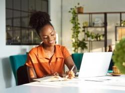 Business woman at desk, writing on a piece of paper in front of her computer.